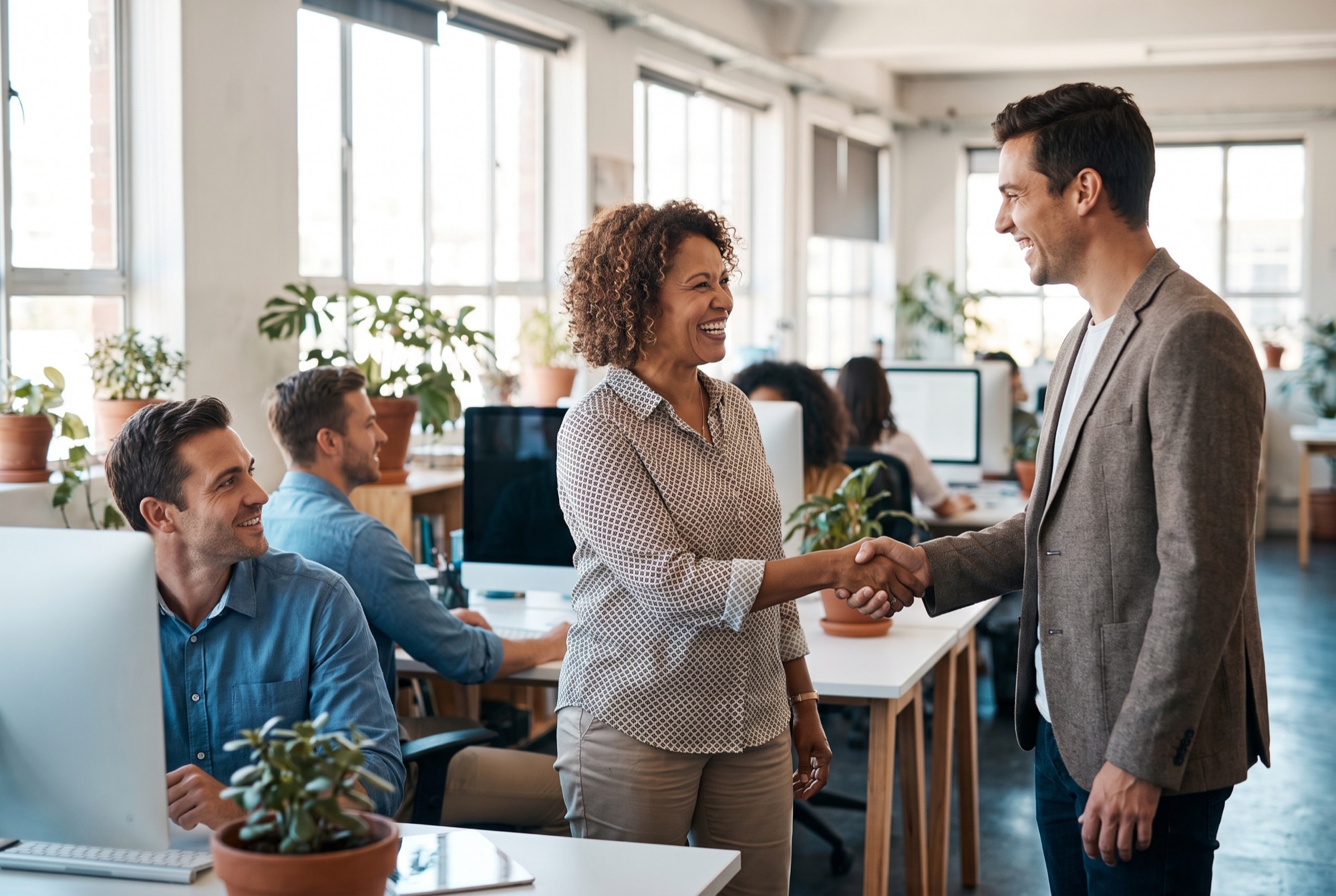 A manager welcoming a new colleague on their first day in an open-plan office.